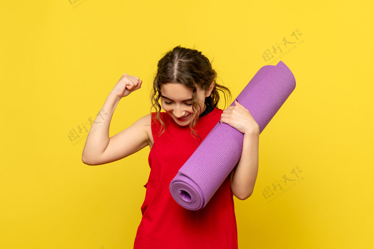 人黄色墙壁上拿着紫色地毯的年轻女子的正视图女性生活方式年轻的女性