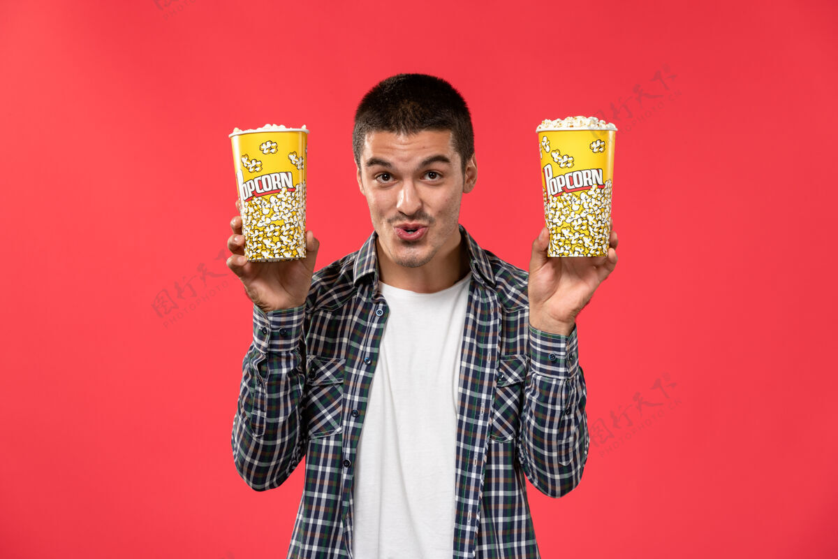 男性正面图年轻男子拿着爆米花包在浅红的墙上电影院看电影观点成人年轻