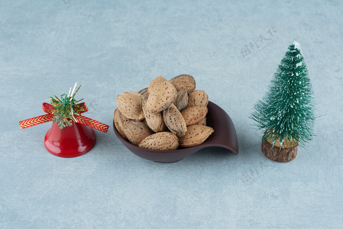 节日一碗去壳的杏仁和大理石上的圣诞装饰品小雕像铃铛天然