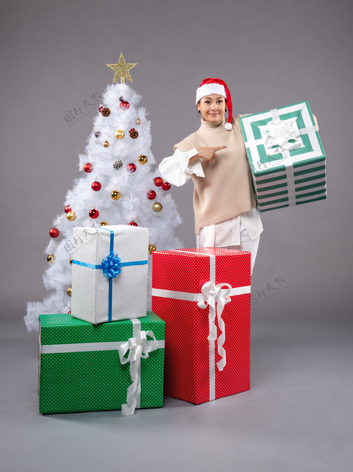 购物年轻的女性在灰色的礼物服装帽子圣诞树