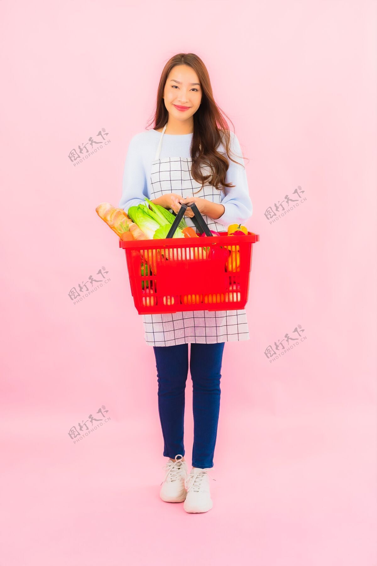 选择一幅美丽的亚洲年轻女子的画像 粉红色的隔离墙上 篮子里放着水果蔬菜和杂货水果购买选择