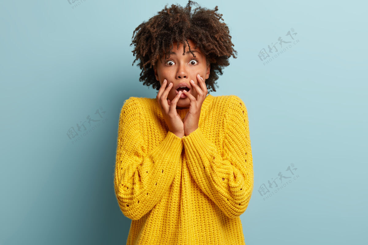 可怕情绪紧张的非裔美国女士屏息凝望 感觉紧张 手靠近脸 眼睛有窃听器 没有安全感 穿着黄色套头衫 站在室内消极情绪种族凝视情绪