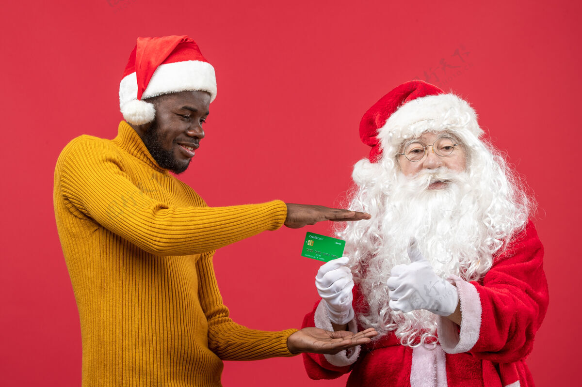 庆祝红墙上的圣诞老人和拿着银行卡的年轻人的正视图快乐年轻男性
