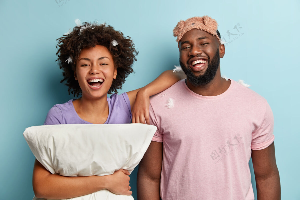 快乐快乐美籍黑人男女真挚欢笑 享受好睡眠 抱着柔软的枕头 戴着睡眠面罩 站得很近 表达好情绪 摆出室内姿势床上用品概念牙齿眼罩民族