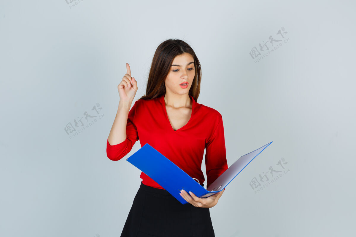 困惑年轻的女士一边看着文件夹 一边指着红衬衫通过女人学生