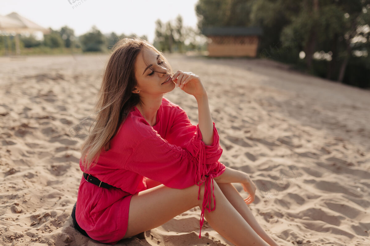 假期穿着粉色连衣裙的迷人时尚的欧洲女人独自坐在沙滩上 享受阳光下的娱乐活动假期时尚夏天