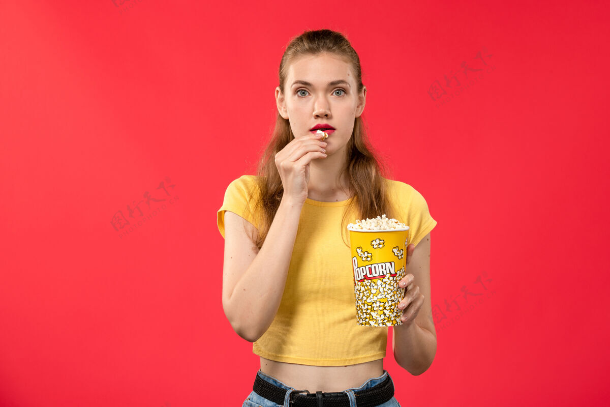 成人正面图年轻女性在电影院拿着爆米花吃红墙电影电影院的女性趣味电影观电影年轻的女性