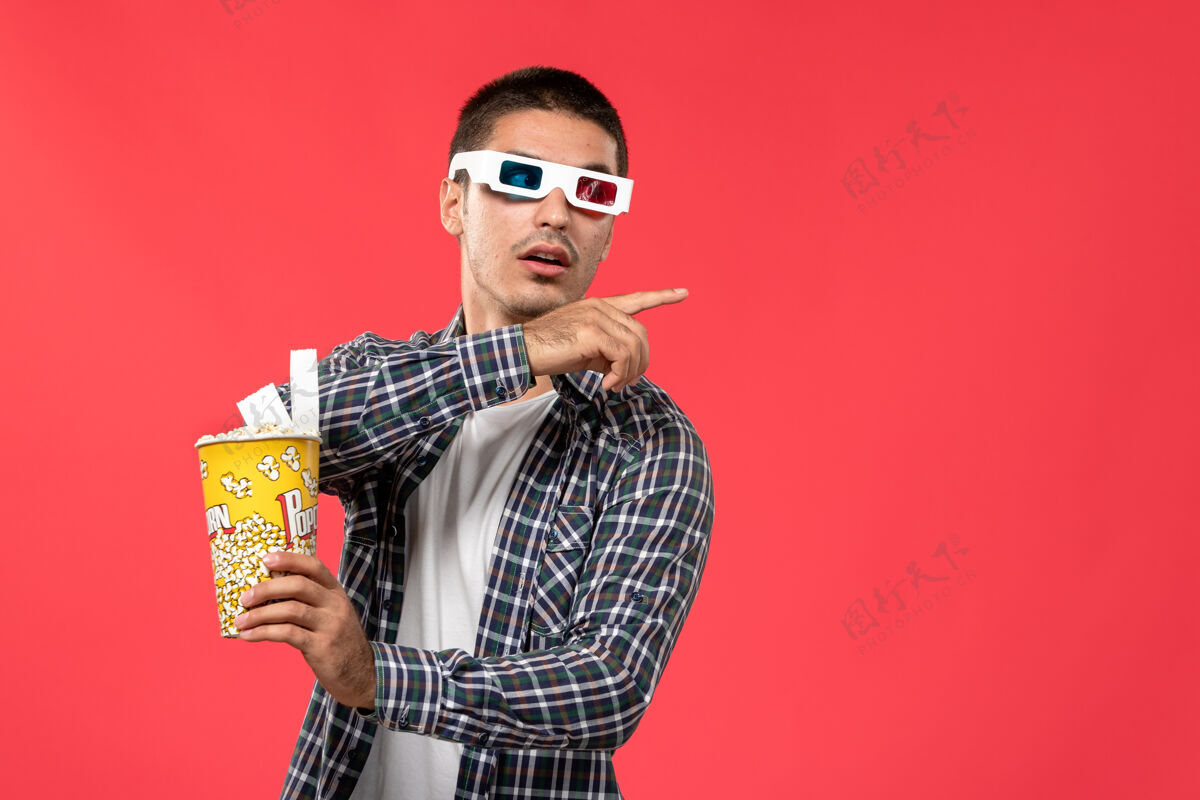 电影正面图年轻男性手持爆米花包在浅红色的墙上 男性电影院的电影欢乐时光年轻时代电影