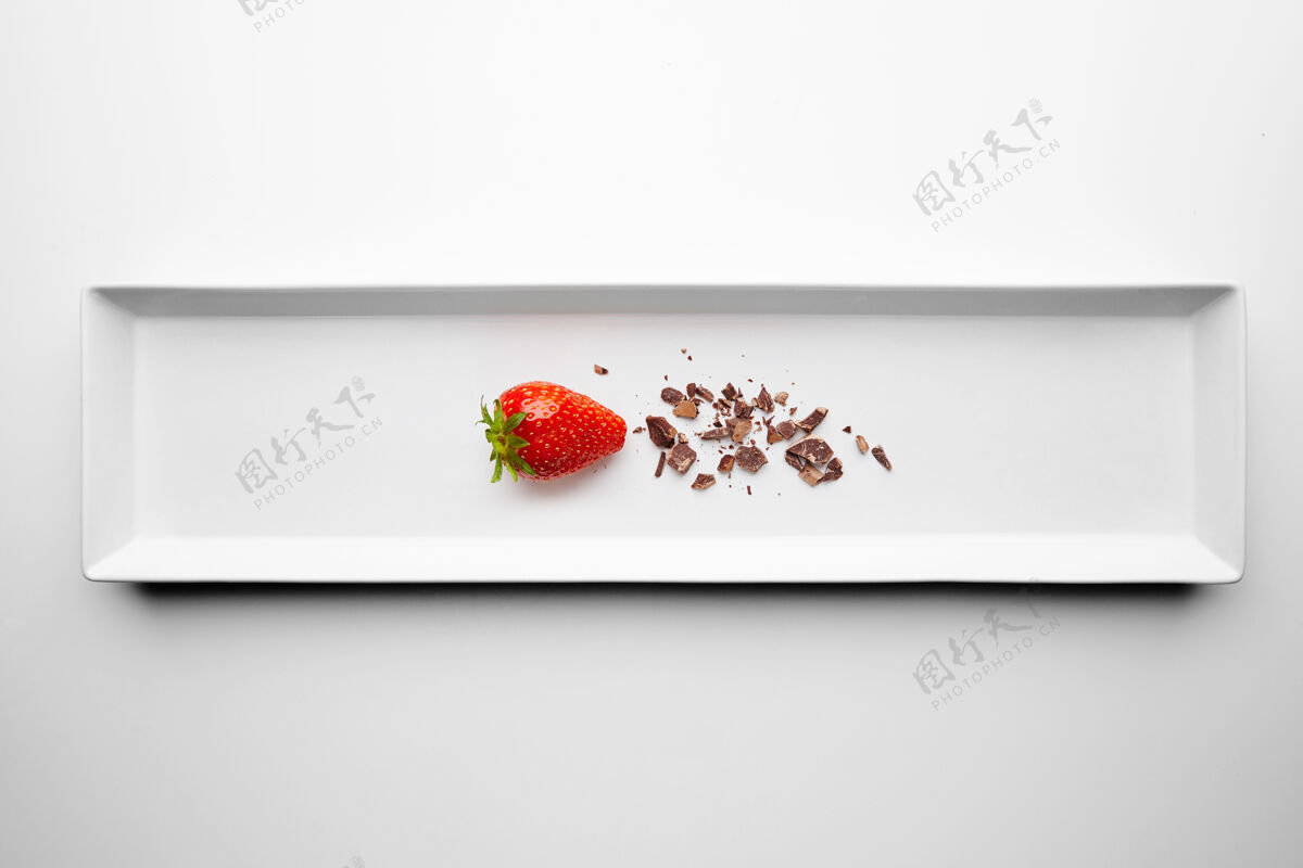 黑熟透的新鲜草莓接近巧克力屑呈现在餐厅的中心矩形陶瓷盘上 在白色背景上独立提供工作室美食巧克力浸泡