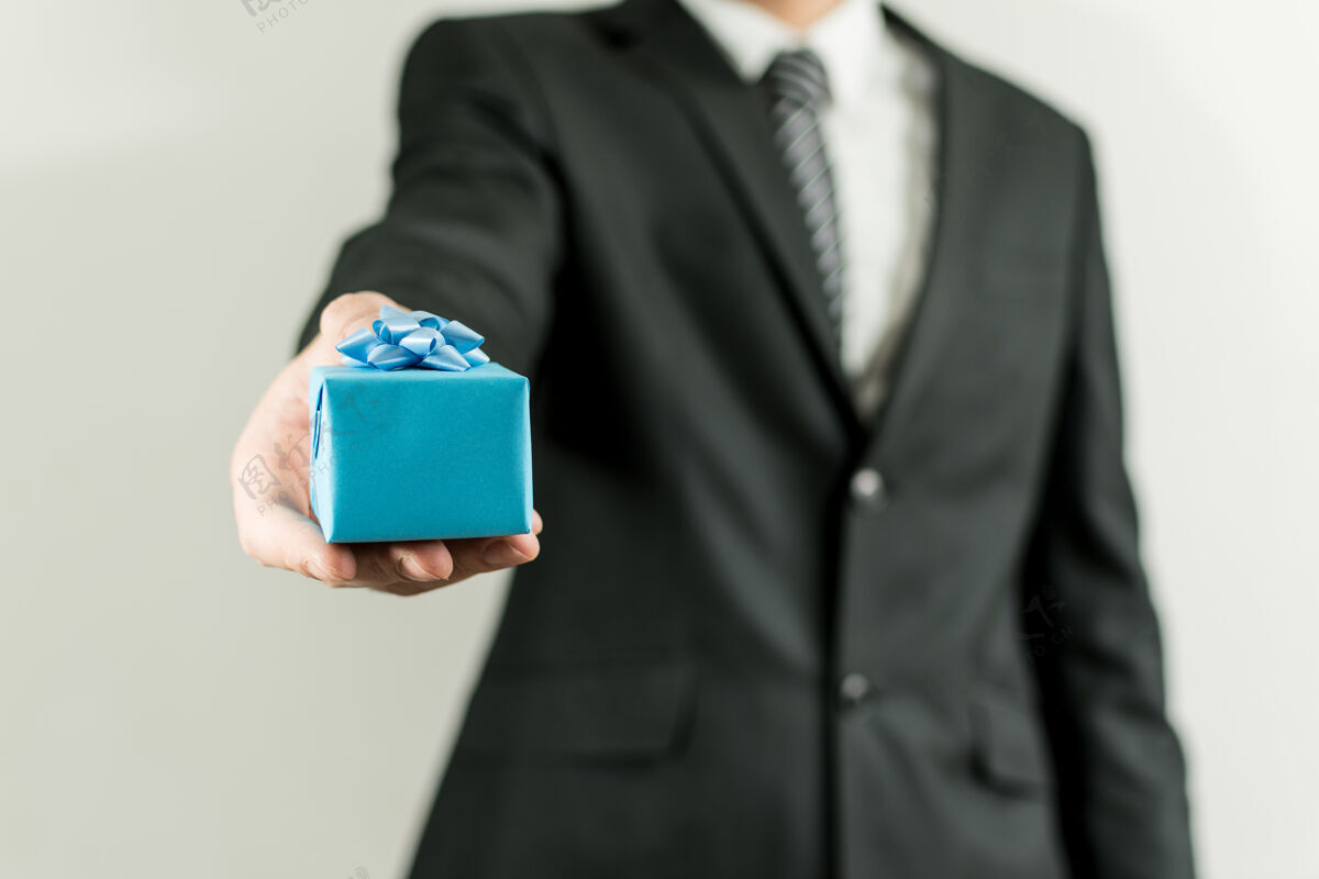 丝带穿西装的男人手里拿着一个蓝色的小礼物盒圣诞节白种人惊喜