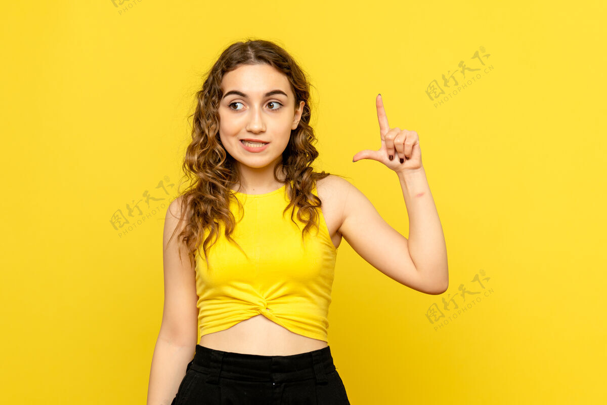 漂亮在黄色墙上摆姿势的年轻女孩的正面图模特情感时尚