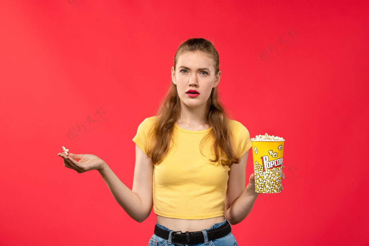爆米花正面图年轻女子在电影院拿着爆米花包和迷茫的淡红墙电影电影院成人视图