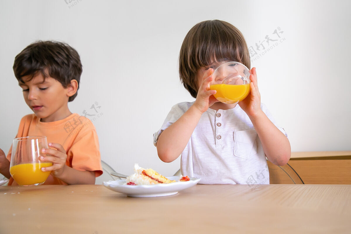 庆祝可爱的小男孩喝着果汁 吃着奶油蛋糕两个可爱的白人孩子坐在餐厅的桌子旁庆祝生日童年 庆祝和节日的概念餐男孩果汁