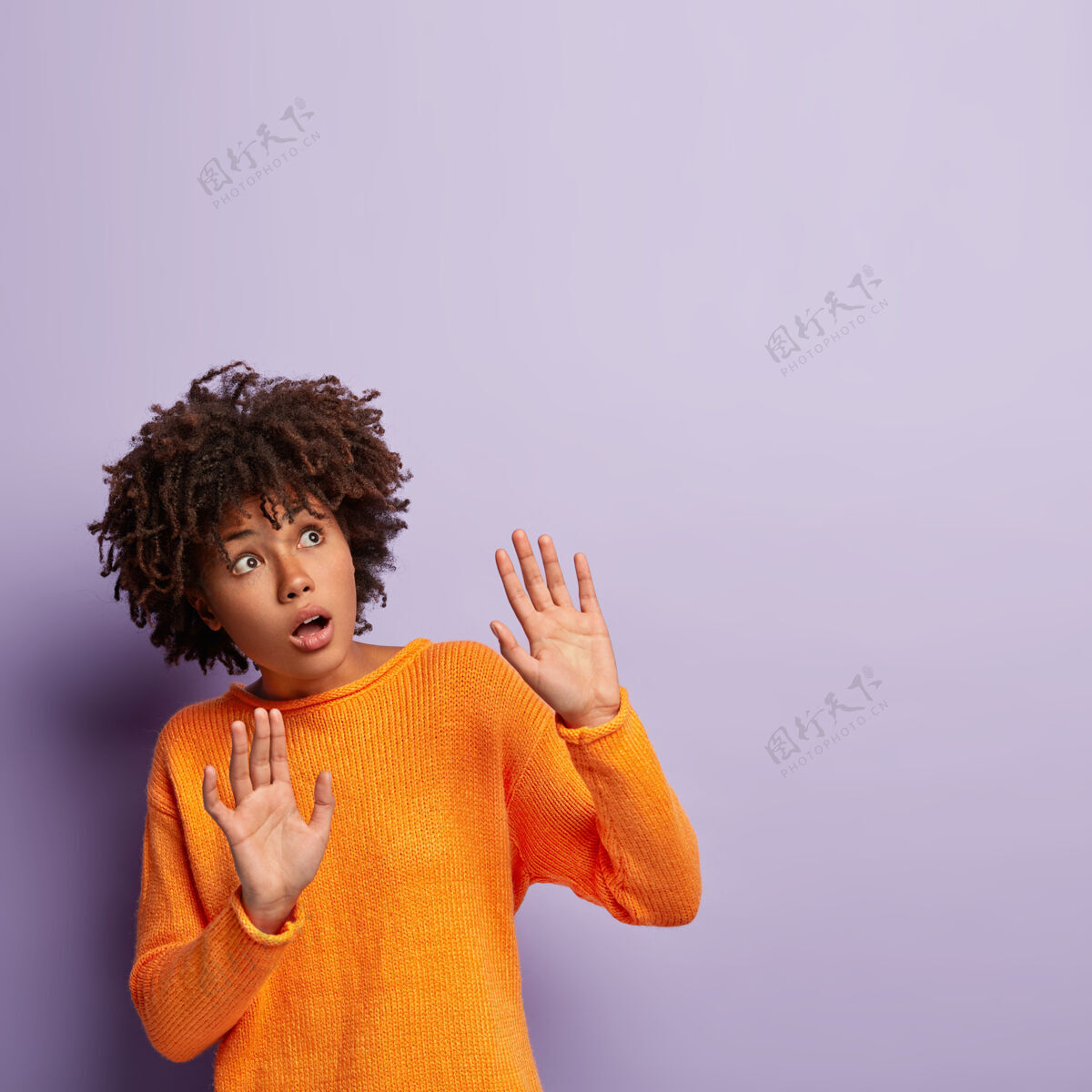 害怕可怕的黑皮肤女性保持手掌向前 试图保护自己 集中在上面 害怕可怕的事情 穿着橙色套头衫 孤立在紫色的墙壁哦不 有东西掉下来了民族惊讶休闲
