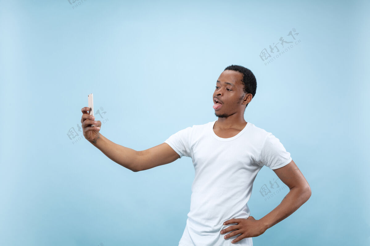 年轻人穿着白衬衫的非洲裔美国年轻人的特写肖像为社交媒体自拍或制作内容 虚拟博客选择媒体顺序