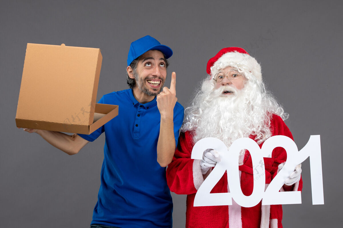 信使圣诞老人的正面图 灰色墙上的男信使拿着购物袋和食品盒庆祝盒子人