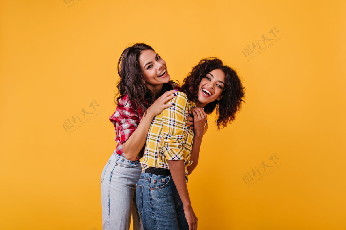 快乐积极的女孩们在黄色的房间里放松 享受拍照的乐趣笑着的棕褐色卷发女孩的画像秋天女人乐趣