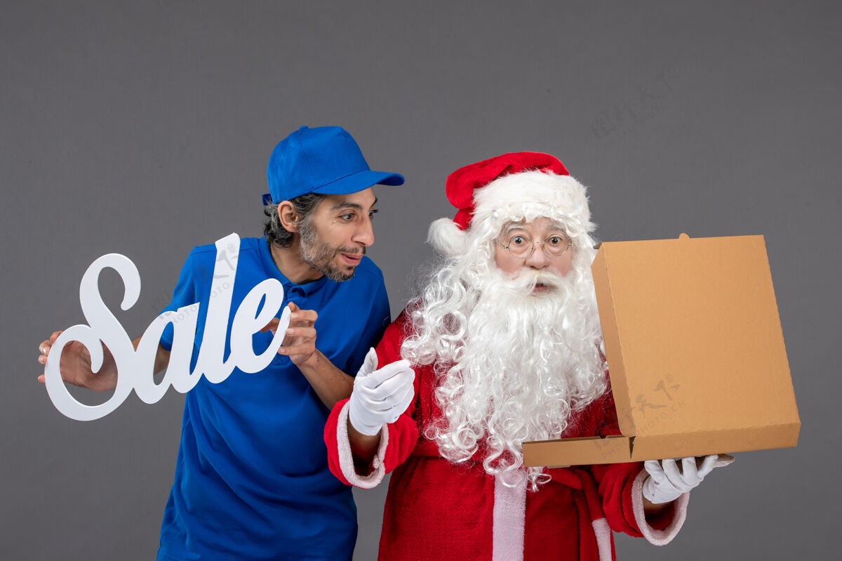 庆祝圣诞老人的正面图 男信使手持销售横幅 打开灰色墙上的食品盒圣诞老人快乐人