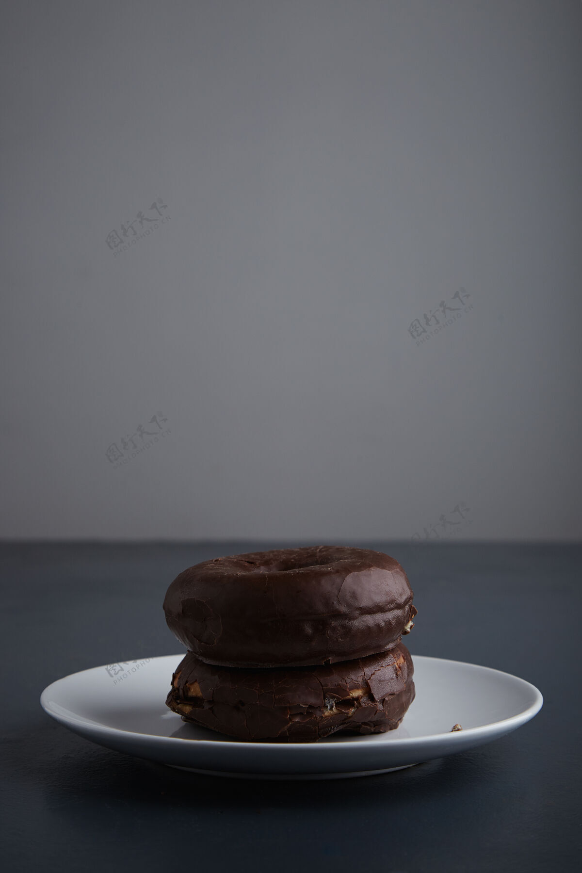 自制两个新鲜出炉的美味甜甜圈 在白色陶瓷小盘上涂上巧克力 放在古朴的蓝色木制桌子上侧视图桌子晚餐不健康