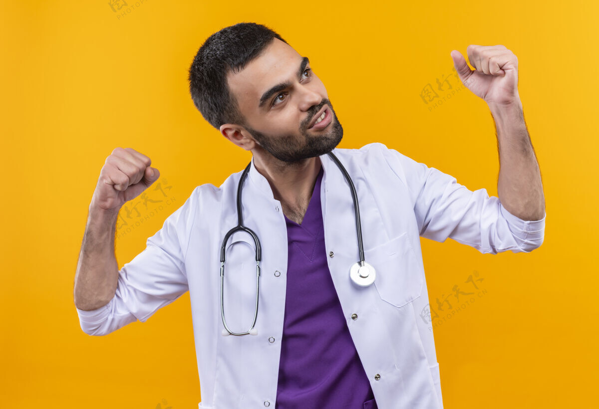 医生看着身边穿着听诊器医用长袍的年轻男医生在孤立的黄色背景上做着强烈的手势听诊器男性手势