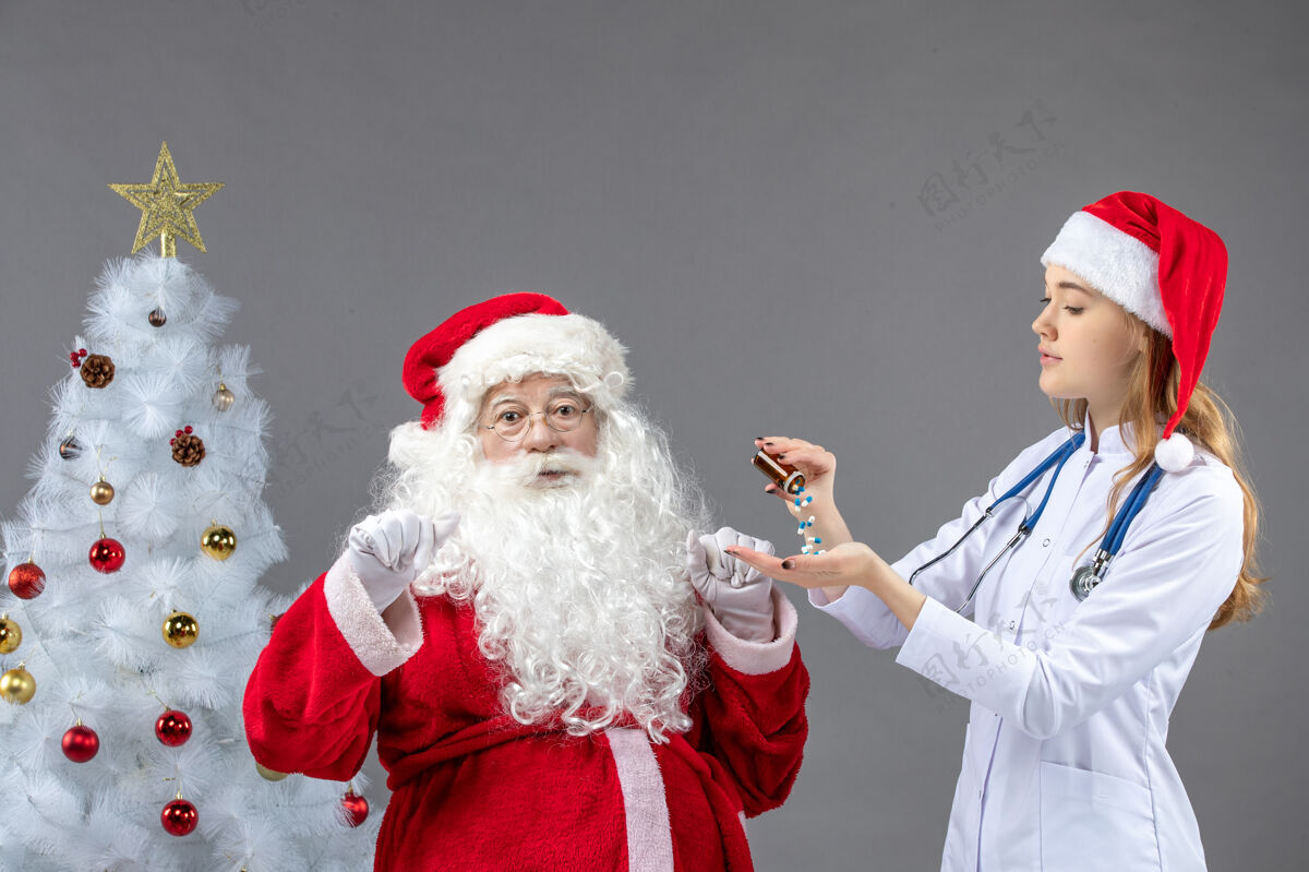 快乐圣诞老人和女医生的前视图 女医生正在灰墙上倒药圣诞老人男人节日