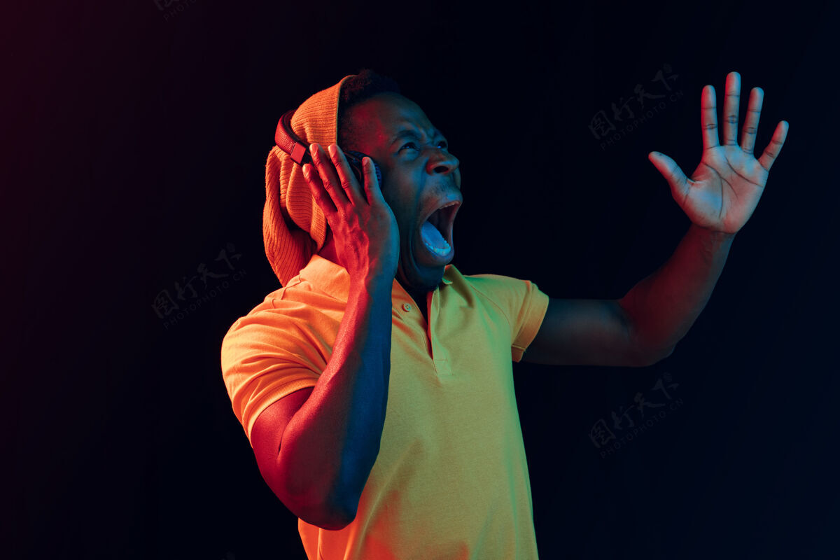 人物年轻帅气的快乐惊喜的时髦男人在霓虹灯下用耳机听音乐迪斯科舞厅 夜总会 嘻哈风格 积极的情绪 面部表情 舞蹈概念美国娱乐说唱
