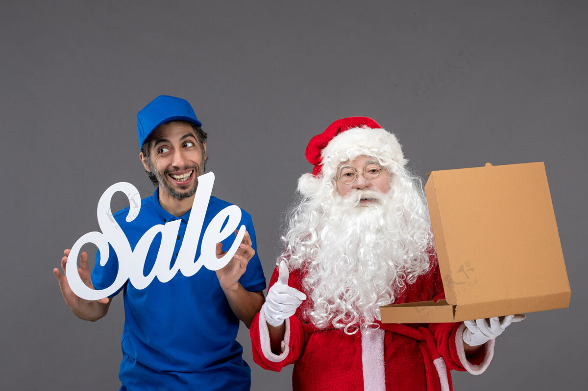 快乐圣诞老人的正面图 男性信使手持销售横幅 灰色墙上有食品盒庆祝食品男人
