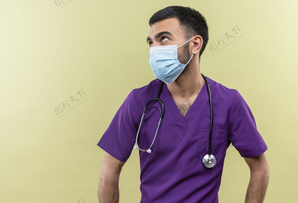 男性看着年轻的男医生穿着紫色的手术服 戴着听诊器医用面罩 背景是孤立的绿色听诊器医疗衣服