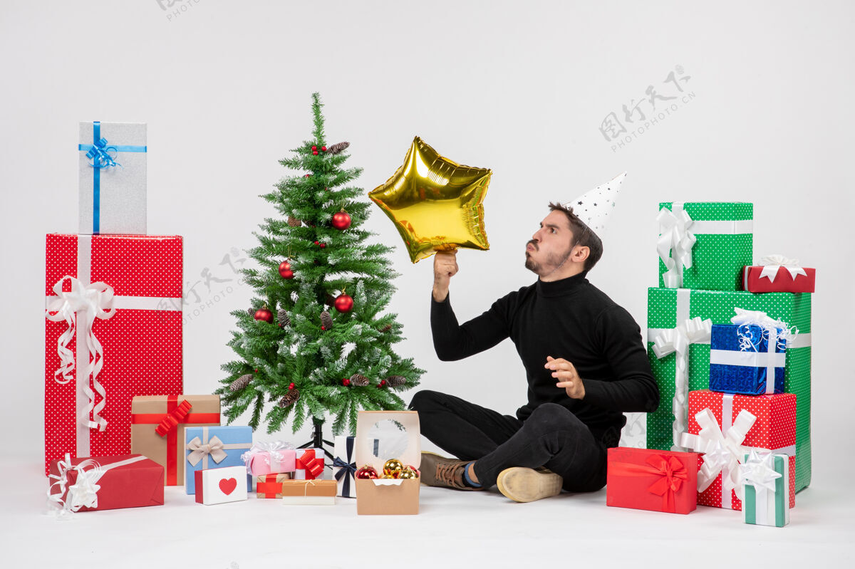 圣诞节年轻人围坐在礼物旁边 拿着金星在白墙上人圣诞快乐庆祝