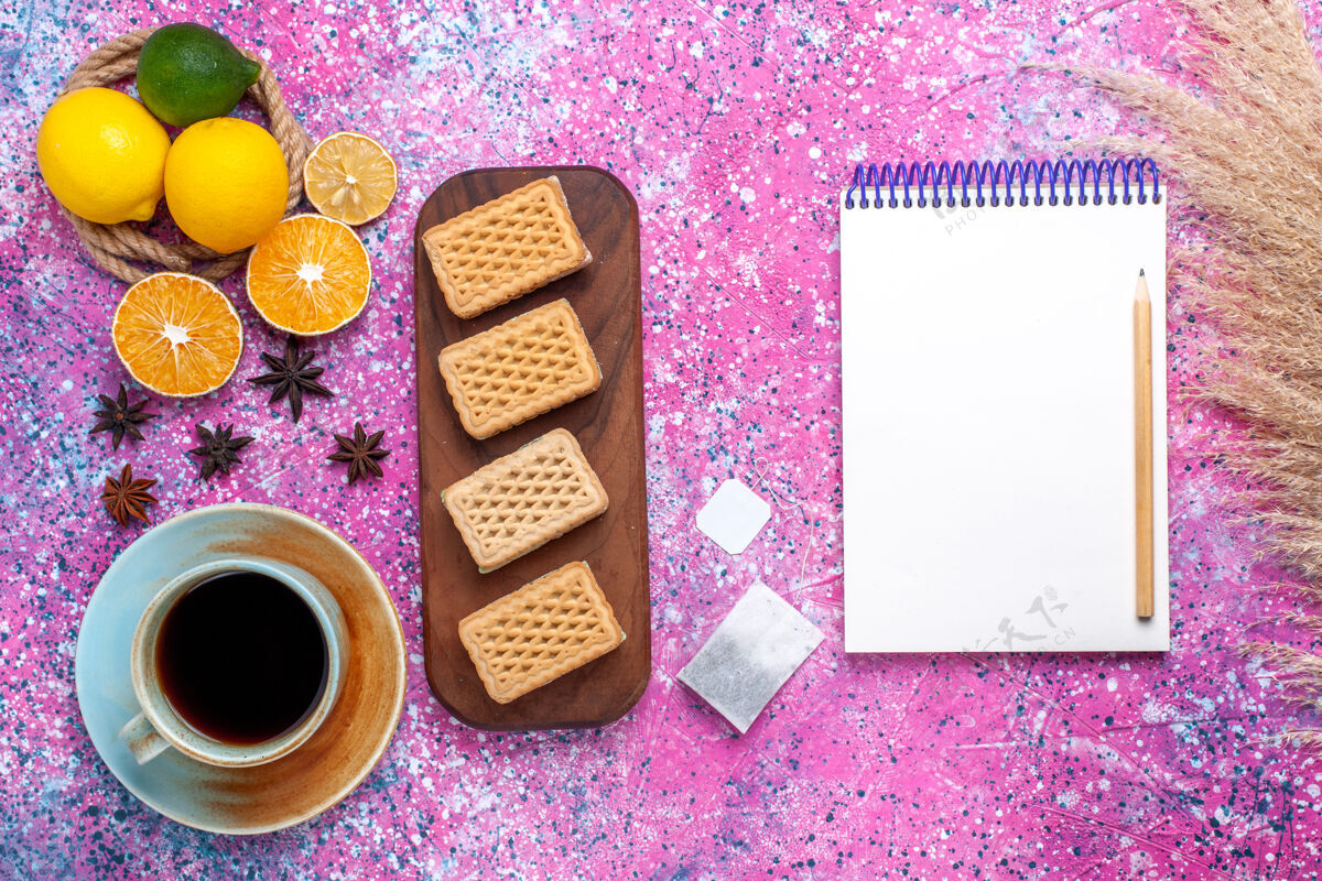 记事本在浅粉色的桌子上可以看到新鲜的黄色柠檬 醇香的酸水果和华夫饼三明治饼干水果曲奇水果