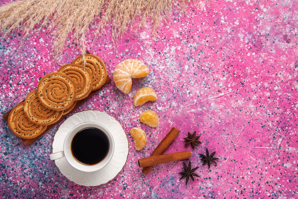曲奇浅粉色的桌子上放着一杯茶 上面放着饼干 肉桂和橘子糖顶部饮料