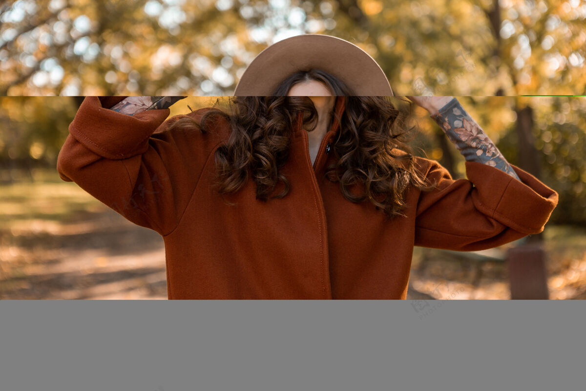 服装画中有魅力的时尚微笑女子留着长长的卷发漫步在公园里穿着温暖的棕色外套秋日时尚 街头风格戴着帽子年轻夹克装束