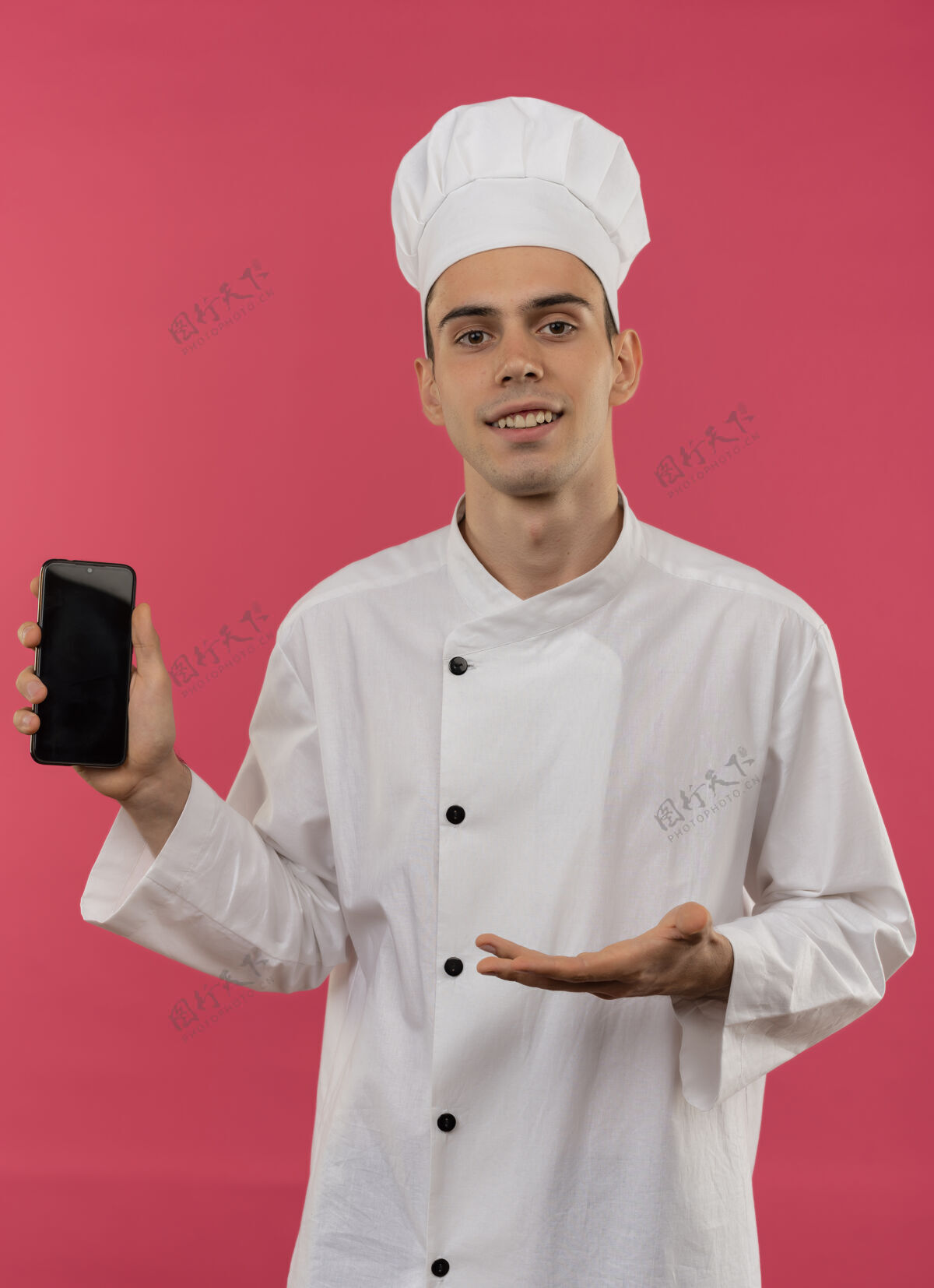 拿着面带微笑的年轻男厨师手拿厨师制服 用手指着电话戴着电话手
