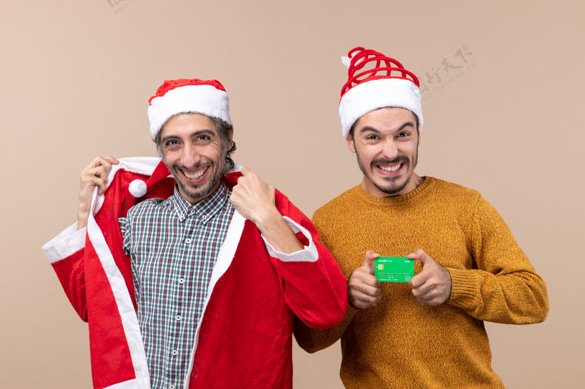 圣诞老人前视图两个快乐的家伙一个穿着圣诞老人的外套 另一个在米色的背景上有信用卡伙计们米色快乐