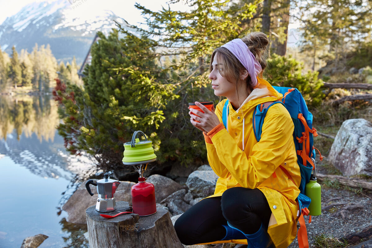 森林体贴的旅行者在山湖边喝着一次性杯子里的热饮 思绪万千炉子享受工具