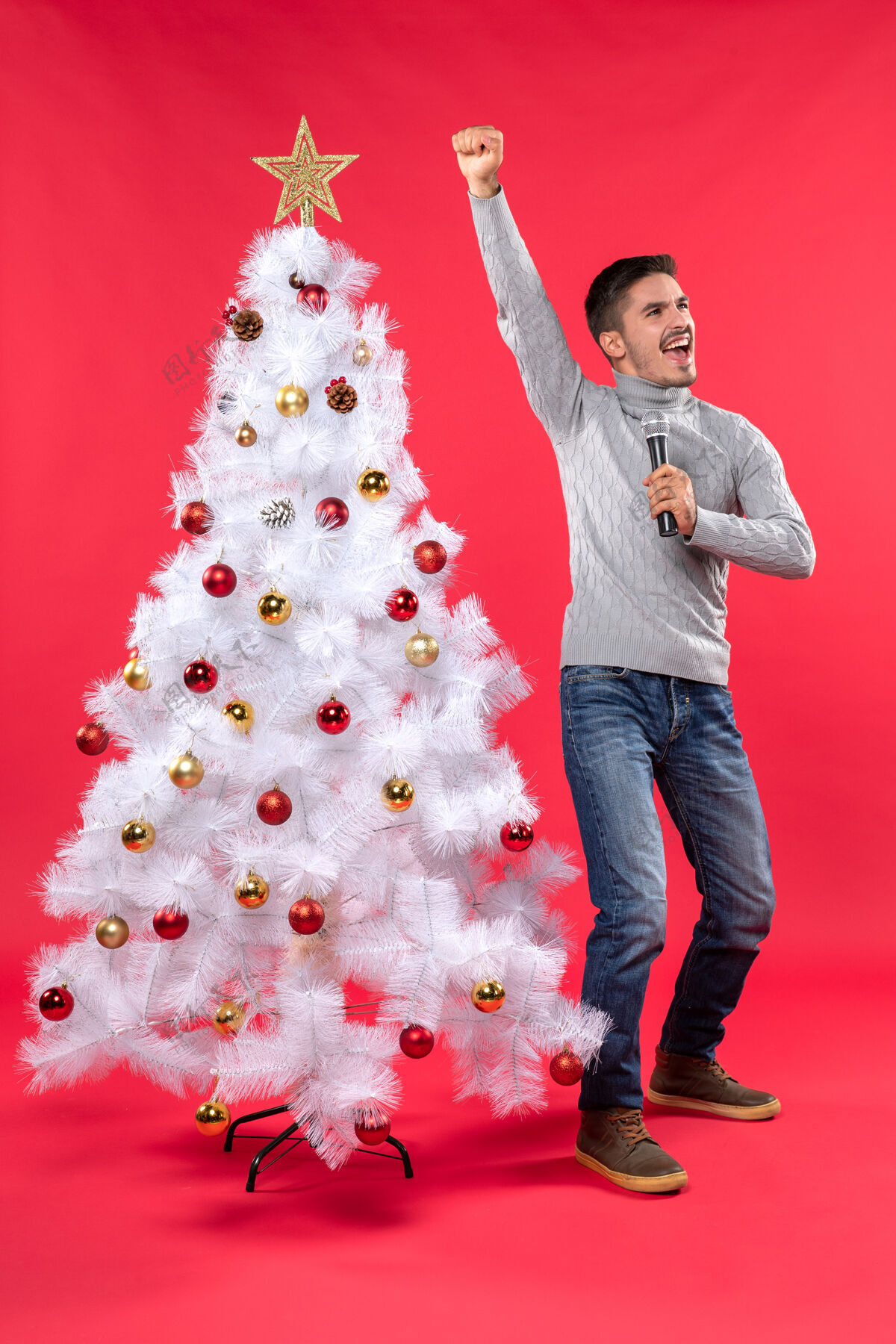 快乐圣诞节心情自信的家伙穿着牛仔裤站在装饰圣诞树附近 为自己感到骄傲快乐自信的男人漂亮