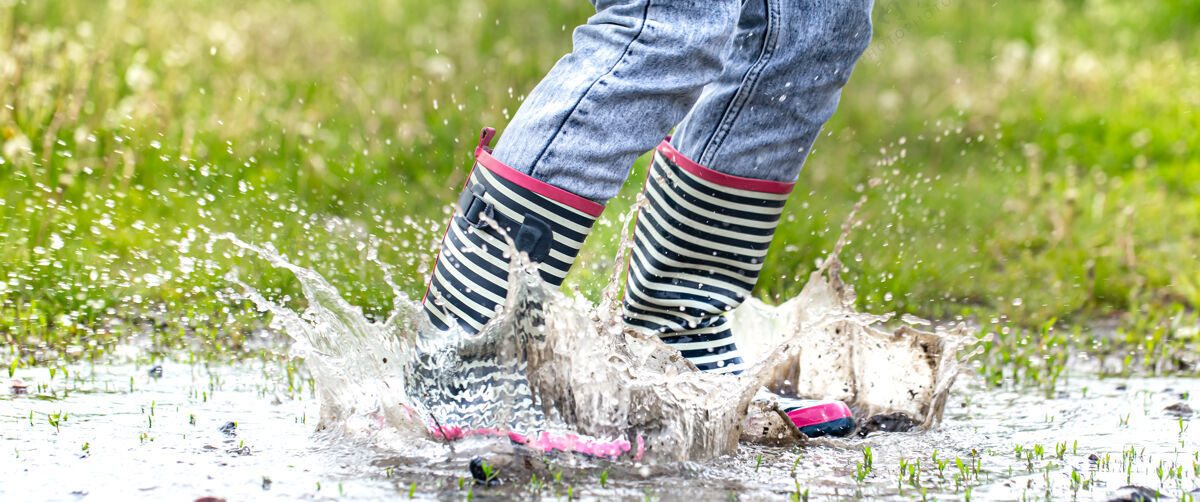 橡胶胶靴在水坑里跳跃的过程中伴随着水花飞溅雨散步雨