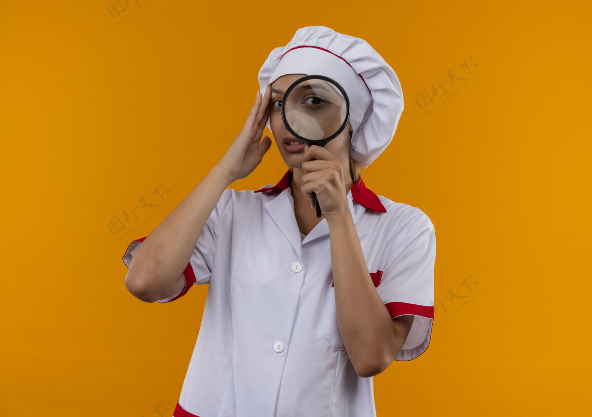 厨师想着年轻的厨师 穿着厨师制服 手放在额头上 用放大镜看着镜头 背景是孤立的橙色女额头手