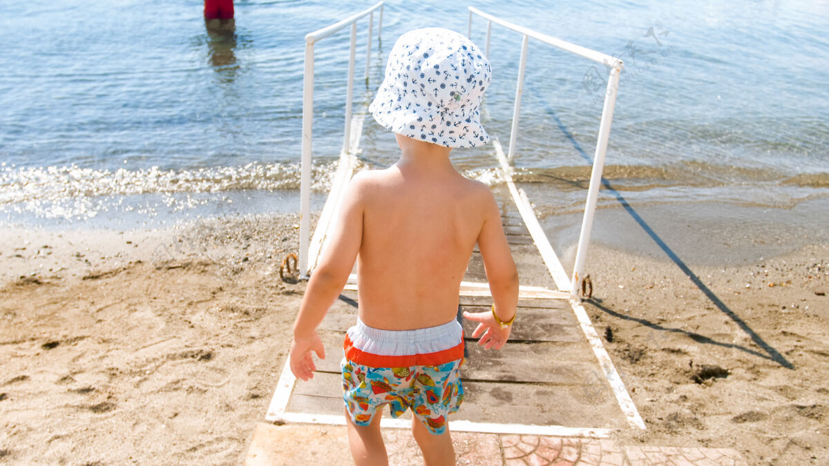海岸戴着帽子的小男孩在沙滩上的海水里散步脚趾海洋水