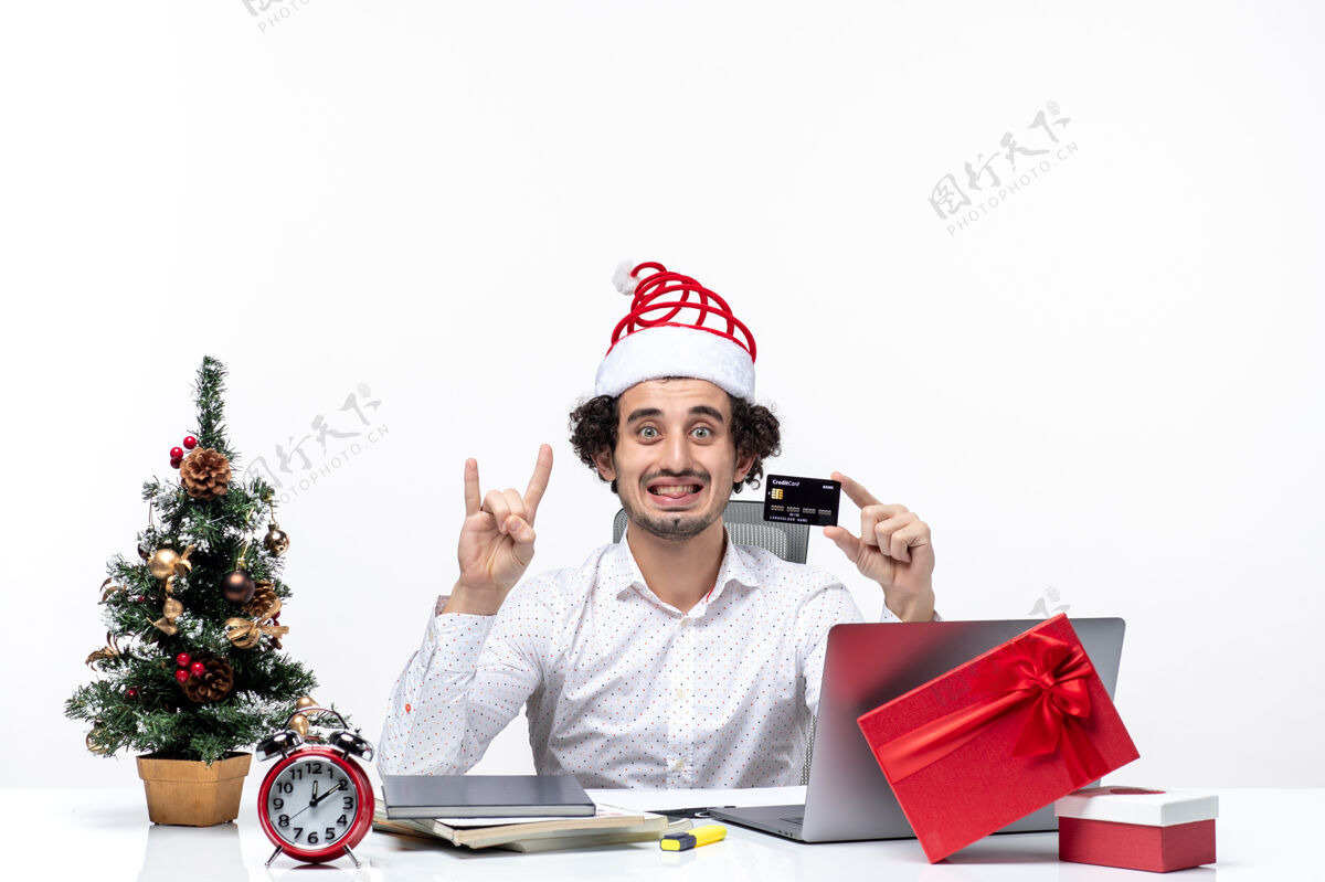 男性圣诞节心情与年轻的胡须微笑的商人与圣诞老人帽子举行银行卡和显示两个白色背景控股帽子人
