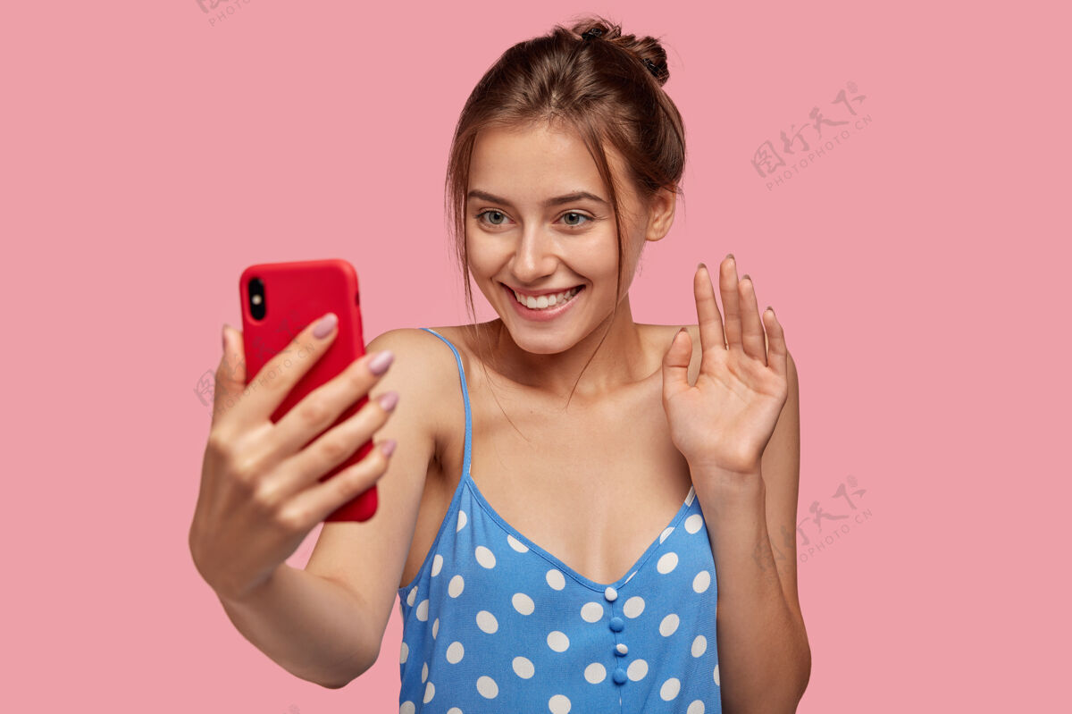 手机高兴的欧洲女人带着愉快的微笑 挥手打手机 身着圆点裙衣服设备衣服