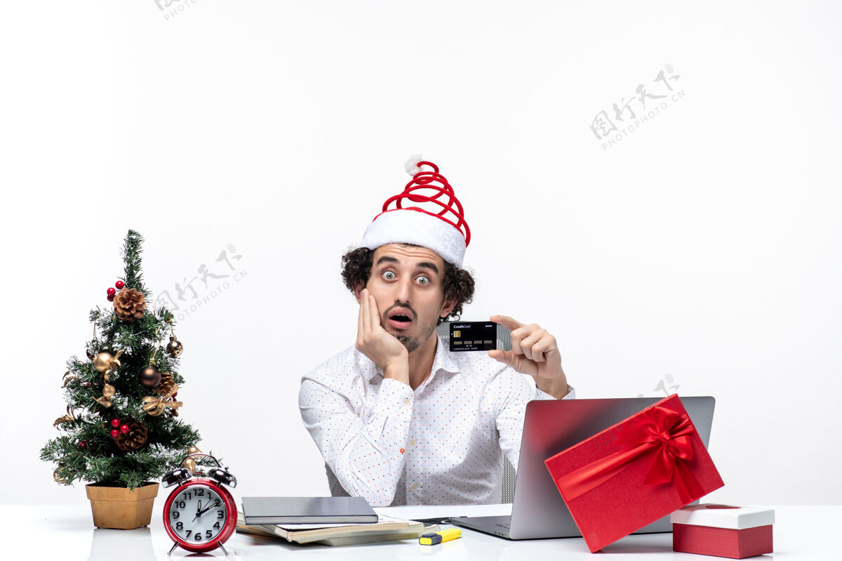 办公室节日喜庆的心情与年轻的胡须震惊商务人士与圣诞老人帽子持有银行卡 并把他的手放在下巴下在办公室下巴手圣诞节