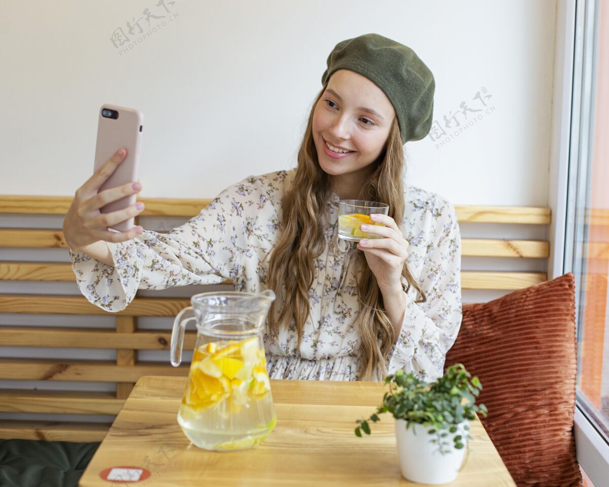 异国情调水果坐在桌边拿着柠檬水杯子自拍的中镜头女人水果美味饮料