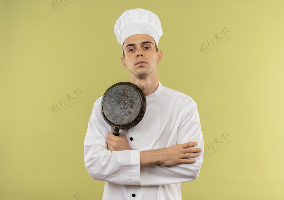 年轻自信的年轻男厨师身穿厨师制服 手拿煎锅 双手交叉放在与世隔绝的绿墙上 留有临摹空间交叉煎厨师