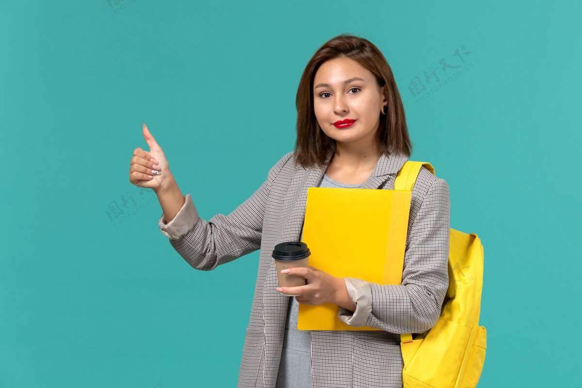 书籍身着灰色夹克的女学生正穿着黄色背包 在淡蓝色的墙上放着文件和咖啡学校前台女学生