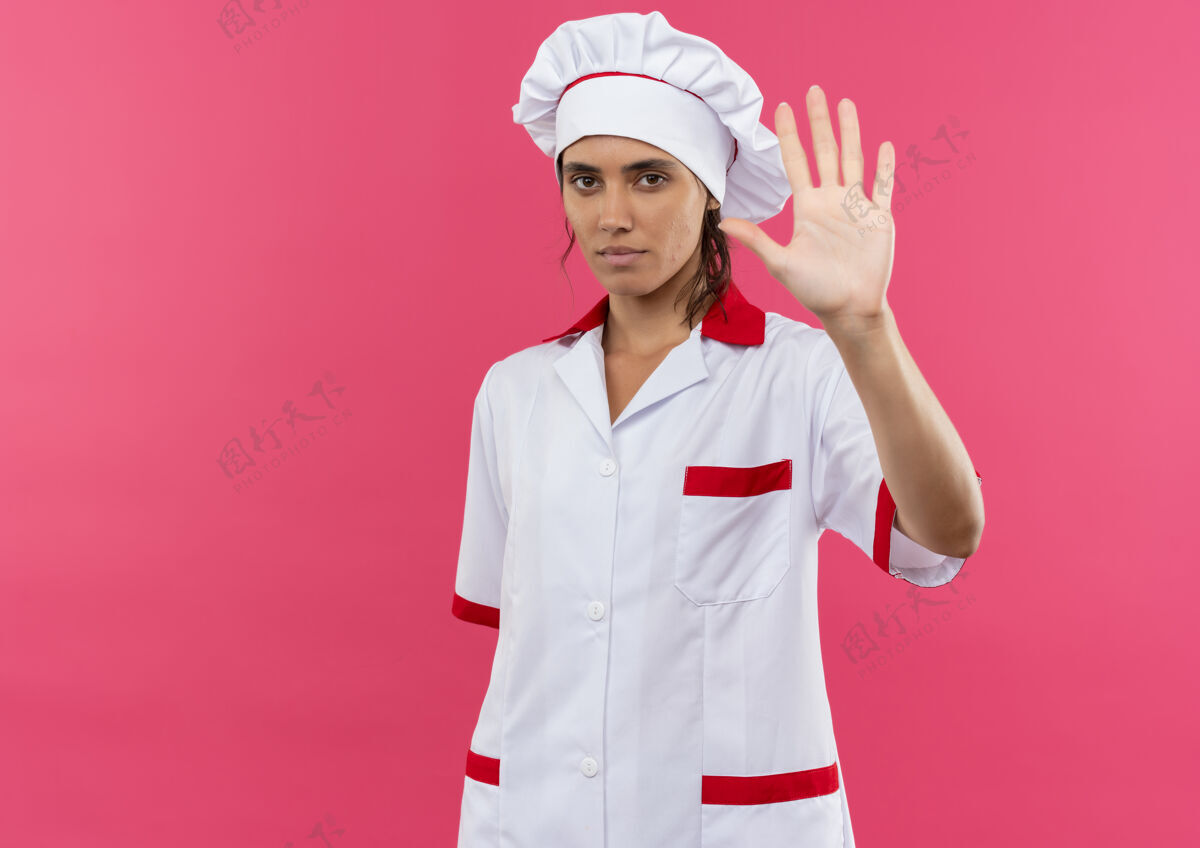 年轻穿着厨师制服的年轻女厨师在隔离的粉色墙壁上展示停止手势 并留有复制空间女表情制服