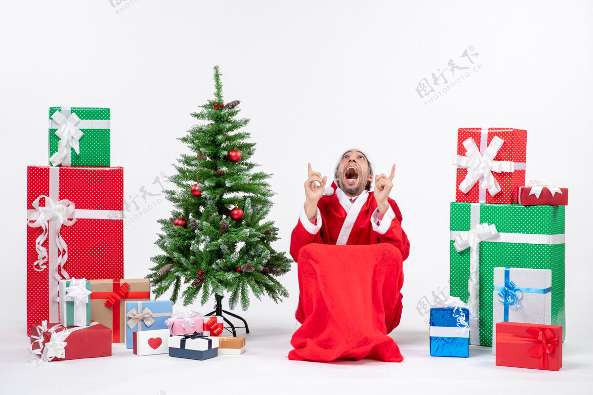 圣诞情绪激动的年轻人打扮成圣诞老人与礼物和装饰圣诞树上的白色背景圣诞老人礼物购物