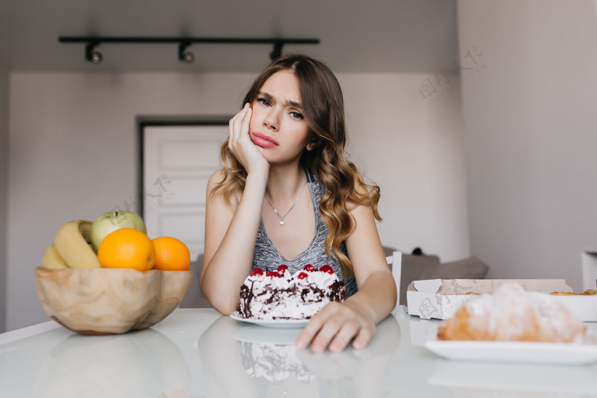 吃失意的女孩早上拿着蛋糕摆姿势欧洲女人在节食时吃水果的室内镜头美味心烦卡路里