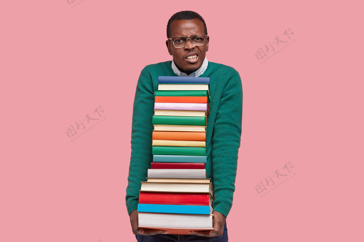 黑暗不满的书呆子咬紧牙关 拿着一堆教科书 戴着大眼镜和绿色毛衣的照片紧握考试男性