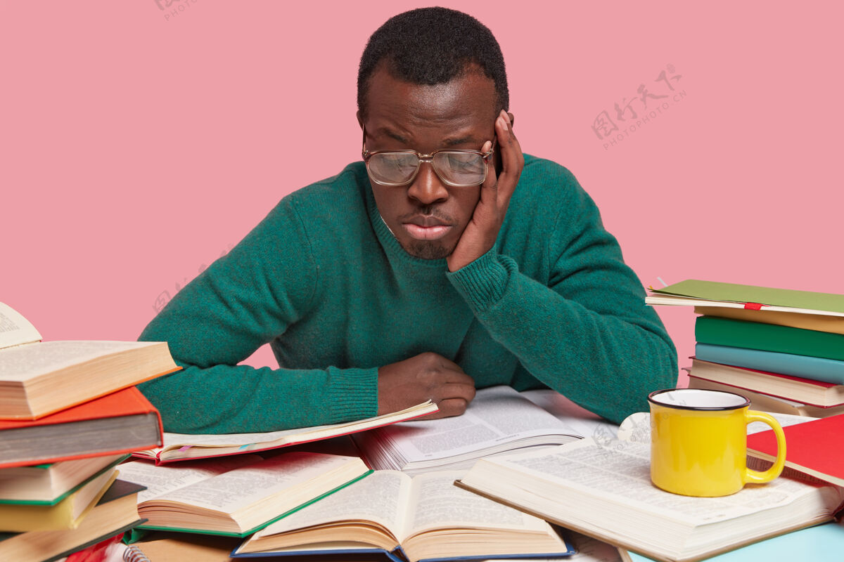 种族专注的黑皮肤男人专注地看手册 学习信息 戴着大眼镜因为视力不好 感到悲伤和无聊百科全书书呆子桌子